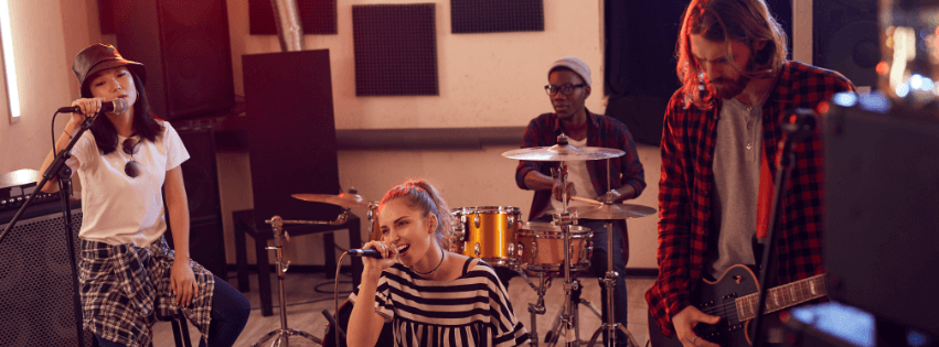 Two ladies singing, one guy playing drums and the other playing a guitar at the rehearsal